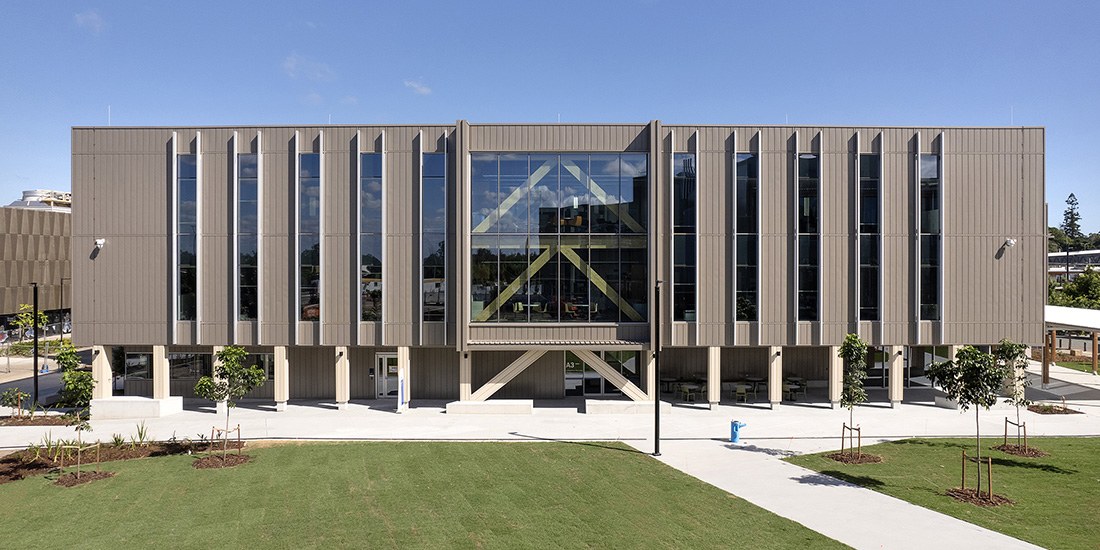 Modern institutional building with vertical metal cladding, large windows, and a geometric facade design set on manicured lawn.