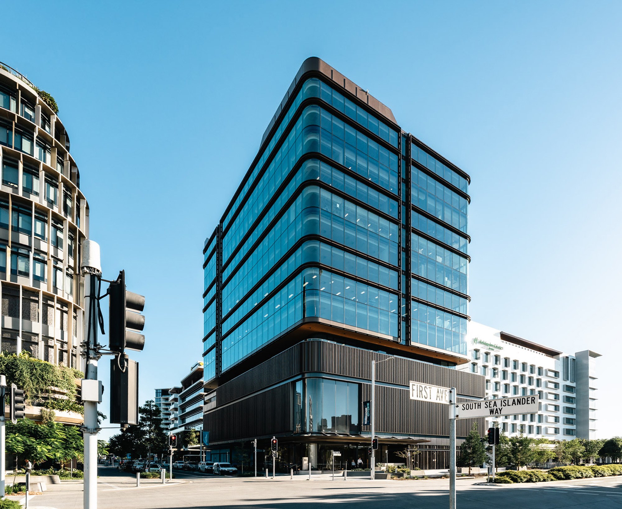 Modern glass-clad office tower with curved balconies at First Avenue and South Slander Way intersection, surrounded by residential buildings.