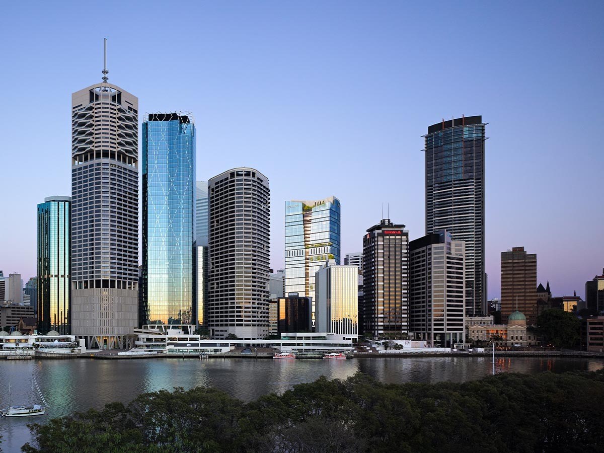 Brisbane skyline at dusk with modern high-rise buildings reflected in the Brisbane River, featuring distinctive cylindrical and rectangular towers.