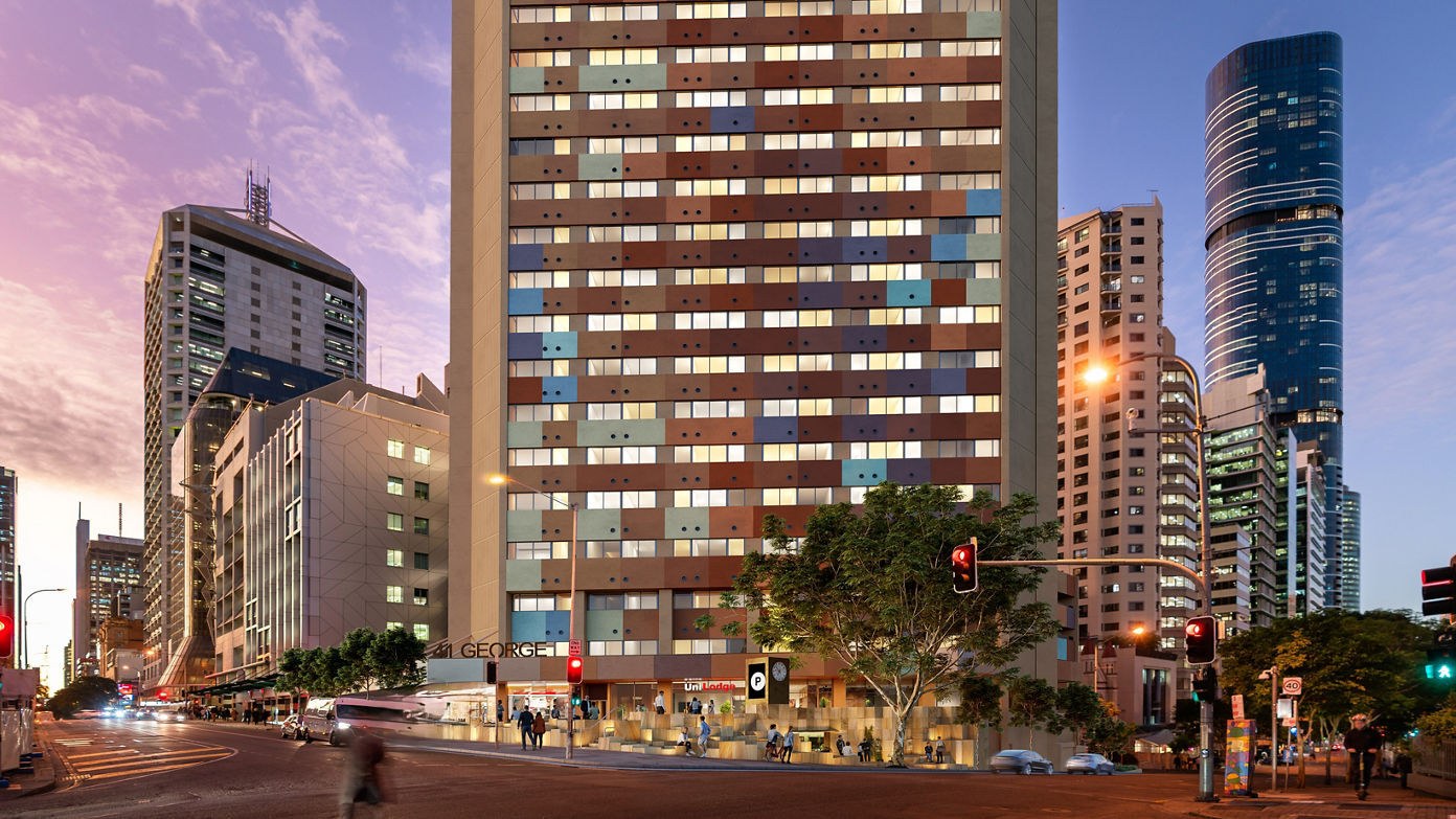 Urban street scene at dusk with tall office buildings, shops, pedestrians, traffic lights, and trees in a city center district.