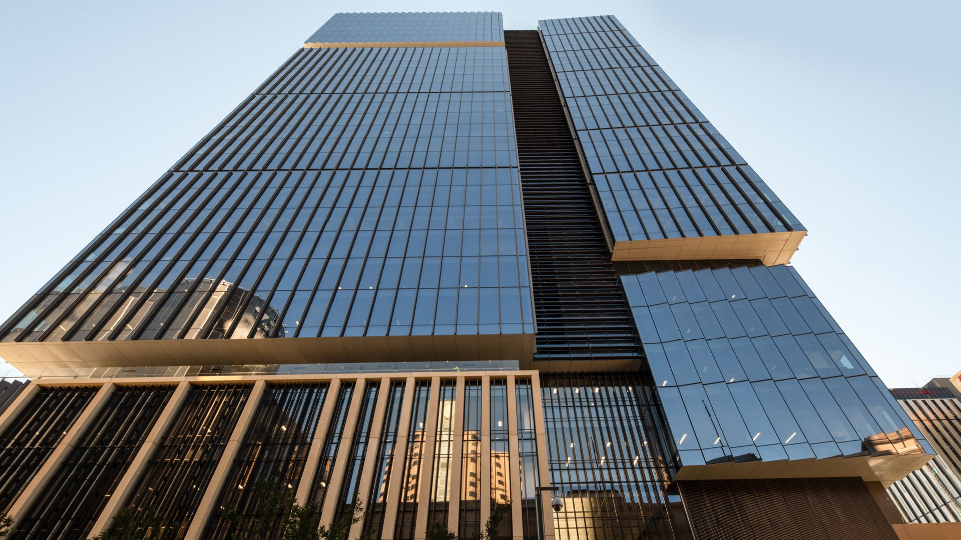 Modern glass and metal skyscraper with horizontal louvers photographed from below against clear blue sky