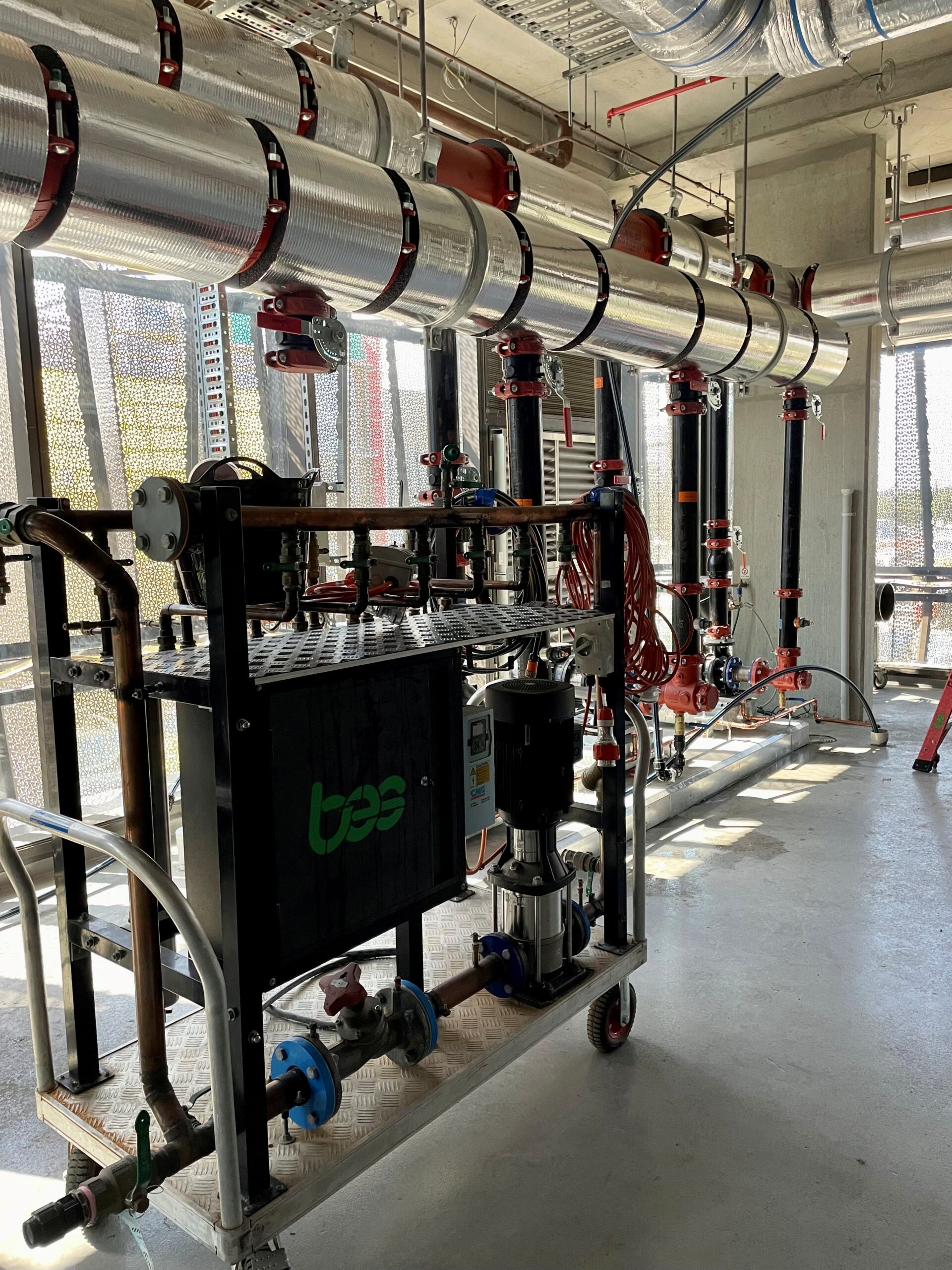 Industrial fire suppression system with red pipes, overhead ducts, and testing equipment in a modern facility with perforated metal panels.
